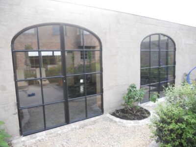 Bijgebouw met dubbelopendraaiende stalen deuren met dubbel glas en mastiek look afwerking. 19. Bijgebouw met stalen deuren